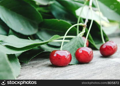 Red cherries and branches with green leaves on a wooden table. Close-up.. Red cherries and branches with green leaves on a wooden table.