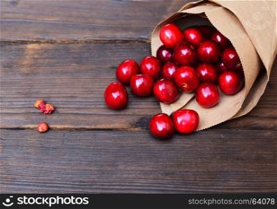 Red cherry in a paper bag on a brown wooden background