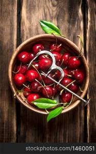 Red cherry in the Cup and metal tool for cherries. On a wooden table.. Red cherry in the Cup and metal tool for cherries.