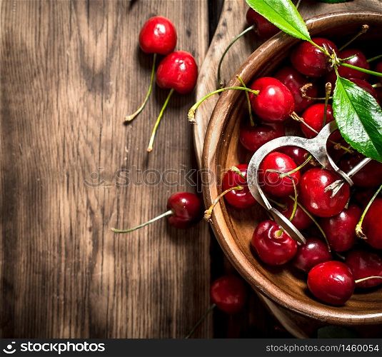 Red cherry in the Cup and metal tool for cherries. On a wooden table.. Red cherry in the Cup and metal tool for cherries.