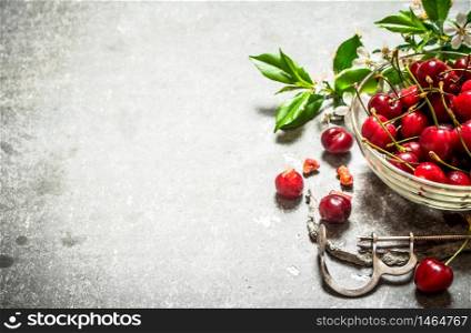 Red cherry in the Cup and metal tool for cherries. On the stone table.. Red cherry in the Cup and metal tool for cherries.