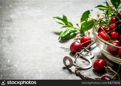 Red cherry in the Cup and metal tool for cherries. On the stone table.. Red cherry in the Cup and metal tool for cherries.