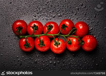 Red cherry tomatoes on a vine isolated on a black wet background. Warer drops on black.. Red cherry tomatoes on a vine isolated on a black wet background.