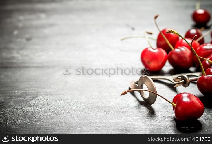 Red cherry with a metal tool to cherry. On a black wooden background.. Red cherry with metal tool