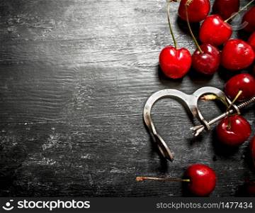 Red cherry with a metal tool to cherry. On a black wooden background.. Red cherry with metal tool