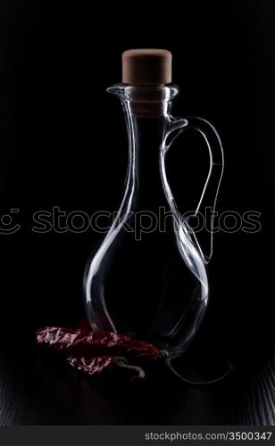 Red chili and a bottle of spiced by a dark background
