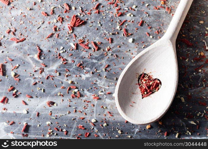 Red chili seasoning in a valentine composition. Wooden spoons with heart-shaped hole. Messy background.. Red chili seasoning in a valentine composition.