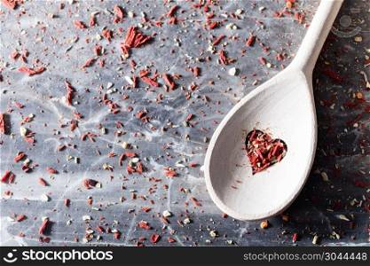 Red chili seasoning in a valentine composition. Wooden spoons with heart-shaped hole. Messy background.. Red chili seasoning in a valentine composition.
