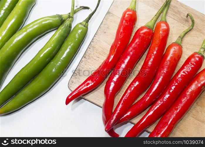 red chilli on cutting board with green chilli on white table,top view
