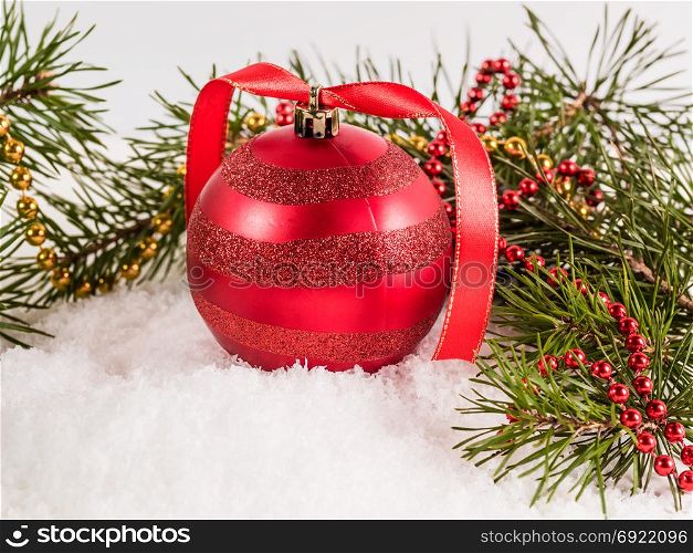 red Christmas ball lying on snow surrounded by fir branches