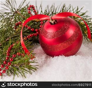 red Christmas ball lying on snow surrounded by fir branches
