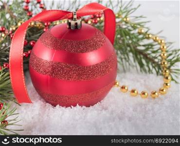 Red Christmas ball with fir branches lying on white snow