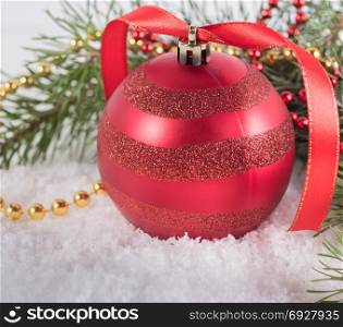 Red Christmas ball with fir branches lying on white snow