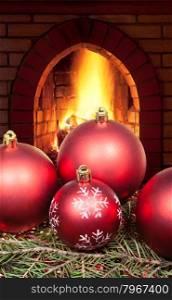 red Christmas balls on green spruce tree with open fire in home fireplace