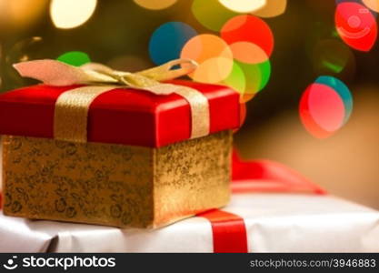 Red Christmas box with golden ribbon on background of colorful lights