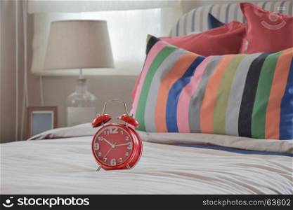 Red clock on white blanket and colourfull striped pillows