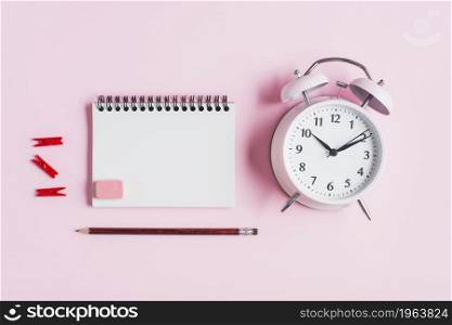 red clothes peg spiral notepad rubber pencil alarm clock against pink backdrop. High resolution photo. red clothes peg spiral notepad rubber pencil alarm clock against pink backdrop. High quality photo