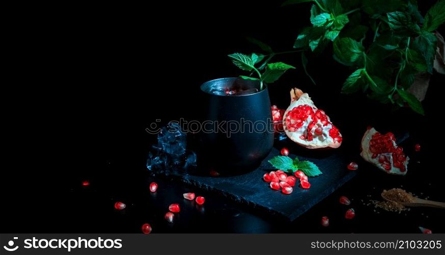Red cocktail with cold vodka and pomegranate juice, ice cubes and rosemary, bar tools, blue black bar counter background, copy space, selective focus