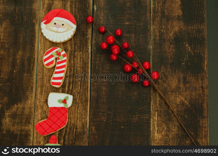 Red cookies for Christmas and a branch with red berries on a wooden background