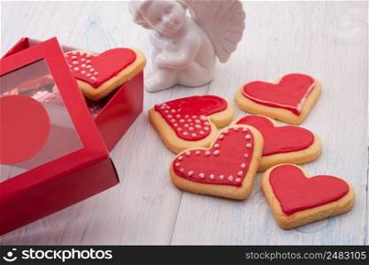 Red cookies in the shape of a heart in a gift box and angels on wooden boards close-up on Valentine’s Day. cookies in the shape of hearts on Valentine’s Day