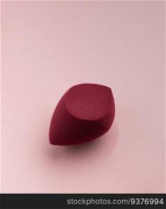 Red cosmetic sponge in the shape of an egg on a pink background. The red cosmetic sponge in the shape of an egg on a pink background