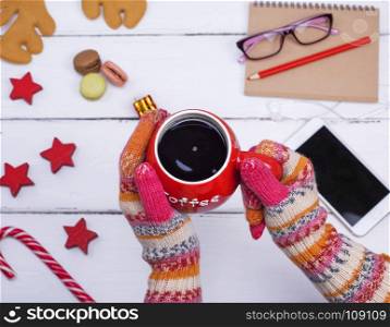 red cup of black coffee in female hands on which knitted winter gloves are dressed, top view