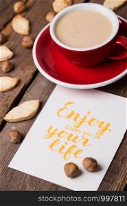 red cup of coffee and leaf shape cookies with the inscription enjoy every day of your life