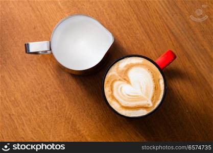 Red cup of latte art coffee on wood table. cup of latte art cappuccino and jug with milk foam on wood table in top view