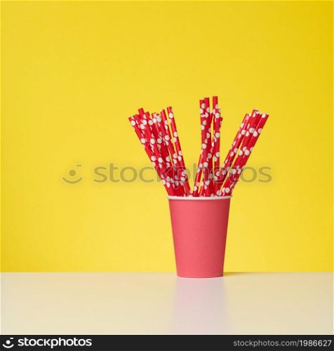 red cup with red paper cocktail tubes on white table, yellow background