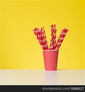 red cup with red paper cocktail tubes on white table, yellow background