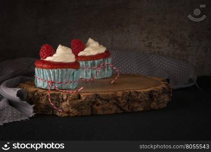 Red cupcakes with cream cheese frosting and raspberries on dark wooden table.