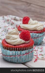 Red cupcakes with cream cheese frosting and raspberries on white wooden table.