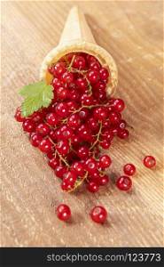Red currant fruits in ice cream cone on wooden table. Focus on leaf.. Red currant fruits in ice cream cone