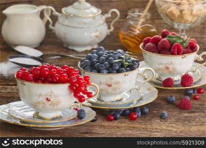 red currant, raspberry and blueberry in cups on wooden table
