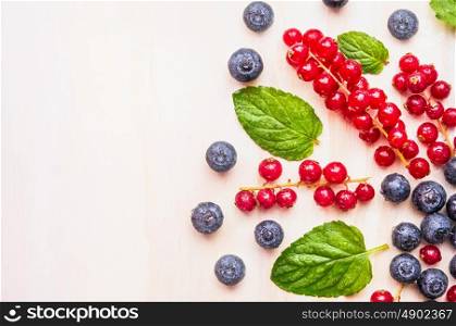 Red currants , blueberries and blackberries with water drops and mint leaves on white wooden background, top view, place for text