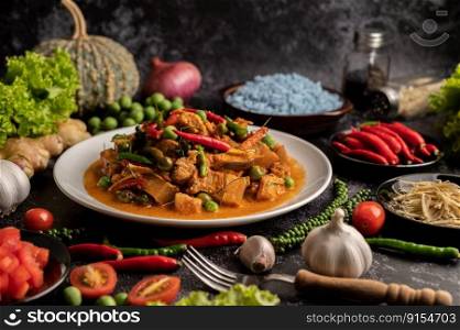 Red curry with pork in a white plate with spices on black cement.