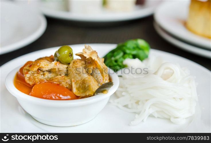 Red curry with roast duck served with vegetable and rice vermicelli on white plate