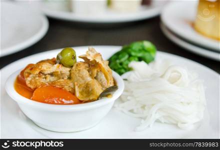 Red curry with roast duck served with vegetable and rice vermicelli on white plate