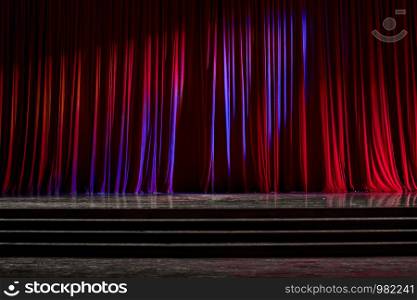 Red curtains and the stage parquet with stairs in theater with colorful lighting.