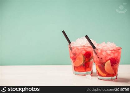 Red drink with ice. Cocktail making bar tools, raspberry, lime, oranges and mint leaves. Raspberry mojito on blue background. Red drink with ice