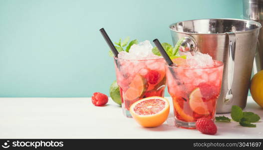 Red drink with ice. Cocktail making bar tools, raspberry, lime, oranges and mint leaves. Raspberry mojito on blue background. Red drink with ice. Red drink with ice