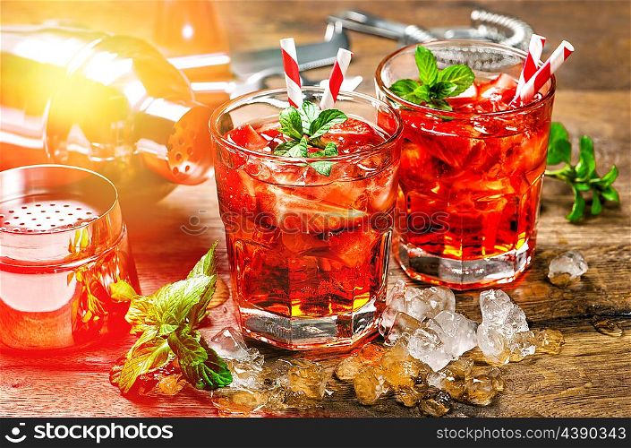 Red drink with strawberry, mint leaves, ice. Cocktail bar with party lights