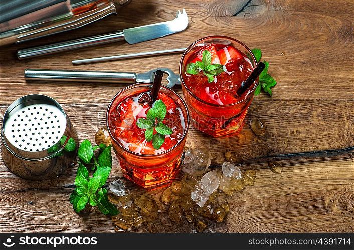 Red drink with strawberry, mint leaves, ice. Shaker and cocktail bar tools
