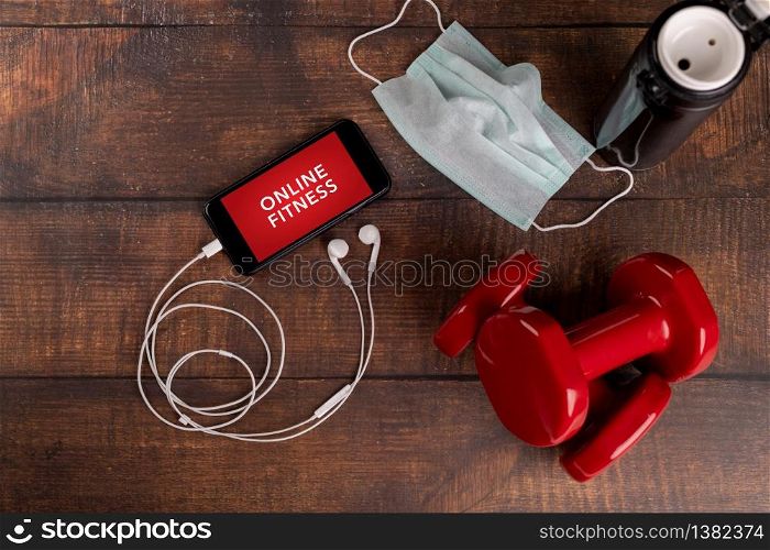 Red dumbbell and smartphone on a woodan background. App for training indoors. Online Fitness program. Home online workout. Top view, Covid-19 Coronavirus quarantine concept. Online fitness program