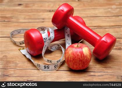 Red dumbbells on a wooden background with a measuring tape and an apple