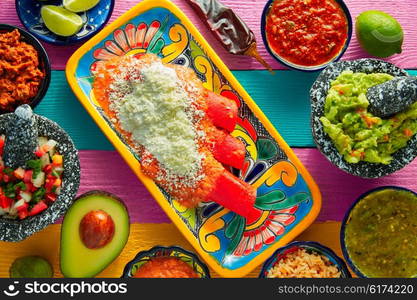 Red enchiladas Mexican food with guacamole and sauces on colorful table