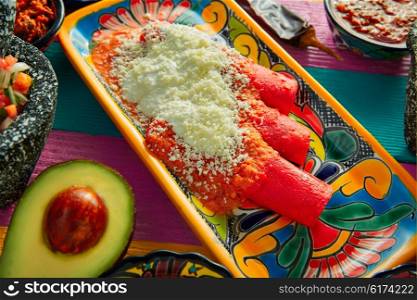 Red enchiladas Mexican food with guacamole and sauces on colorful table