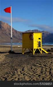 red flag water lifeguard chair cabin in spain lanzarote rock stone sky cloud beach musk pond coastline and summer