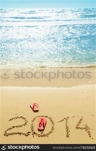 Red flip flops and digits 2014 on the beach sand.Concept of summer vacations and new year