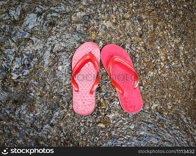 Red flip flops on beach with gravel and water flow wave